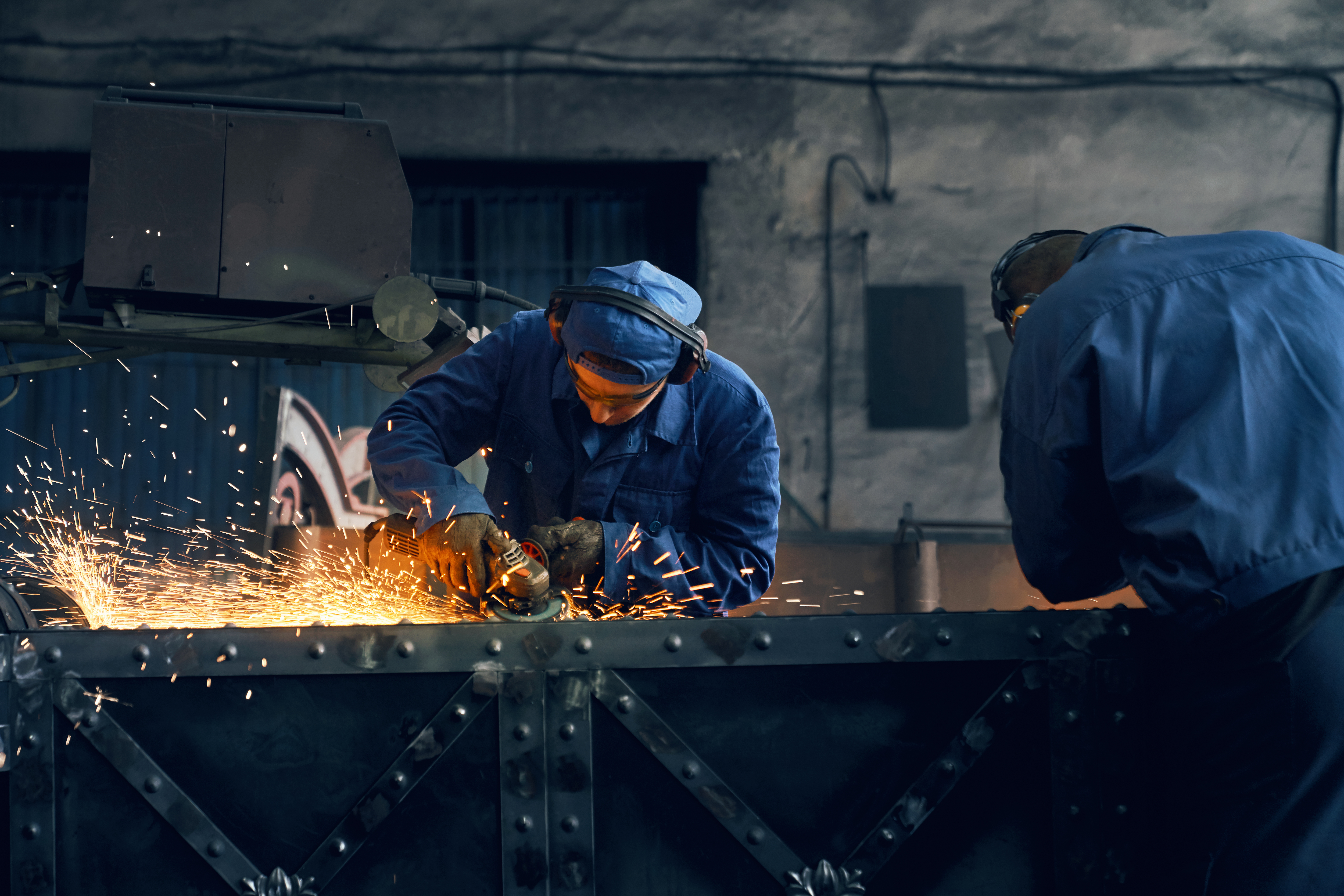 Front view of two men working with special electric steel cutter machine for welding or making gates in smithy. Concept of process produce modern fence in garage.